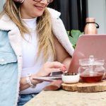 A woman sits outdoors with her laptop, utilizing self-service tools for customer service.
